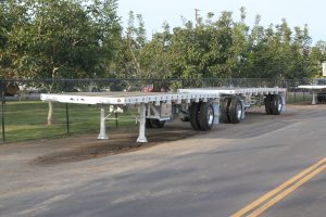 white wesco flatbed trailer set on a road by an orchard