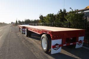 red wesco flatbed trailer set on a road with white mudflaps
