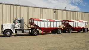 red hopper trailer set pulled by white truck
